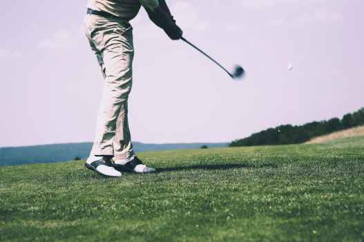 man in white denim pants and black sandals playing golf during daytime