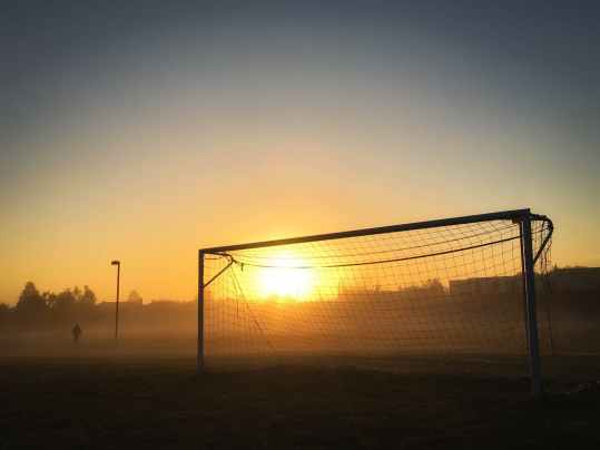 person jogging near soccer goal during sunrise